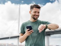 Čovek na treningu gleda u pametni sat i drži telefon