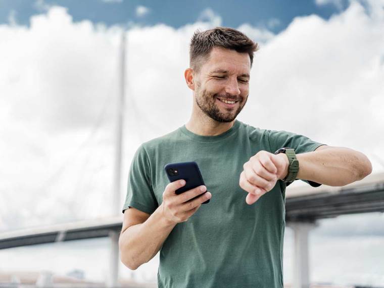 Čovek na treningu gleda u pametni sat i drži telefon